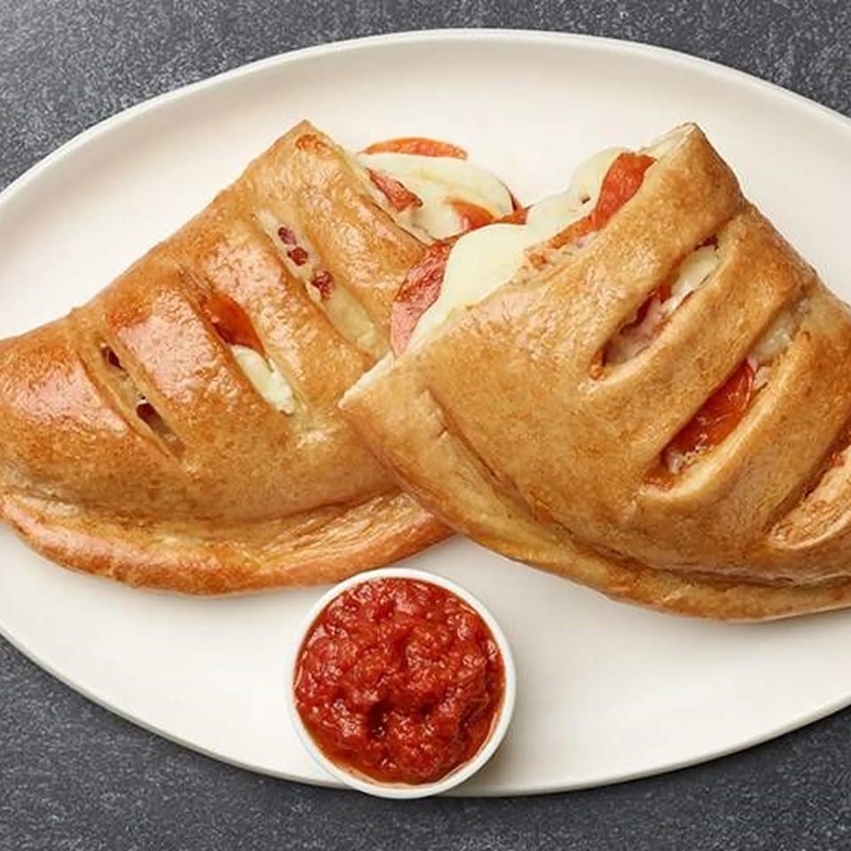 Two golden-brown pepperoni and cheese calzones with a side of marinara sauce on a white plate.