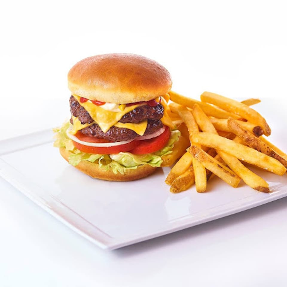 A double cheeseburger with lettuce, tomato, onion, and fries on a white rectangular plate.
