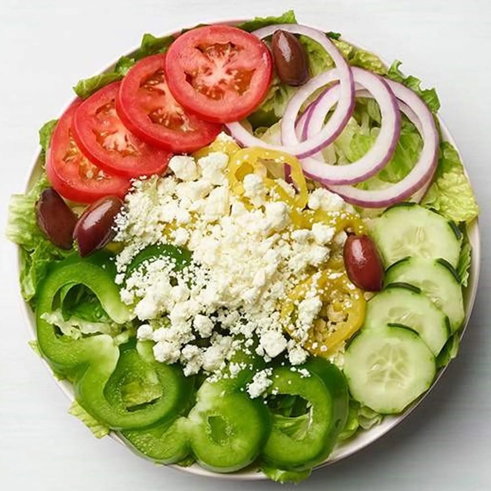 A vibrant Greek salad with lettuce, tomatoes, onions, cucumbers, peppers, feta, and olives.